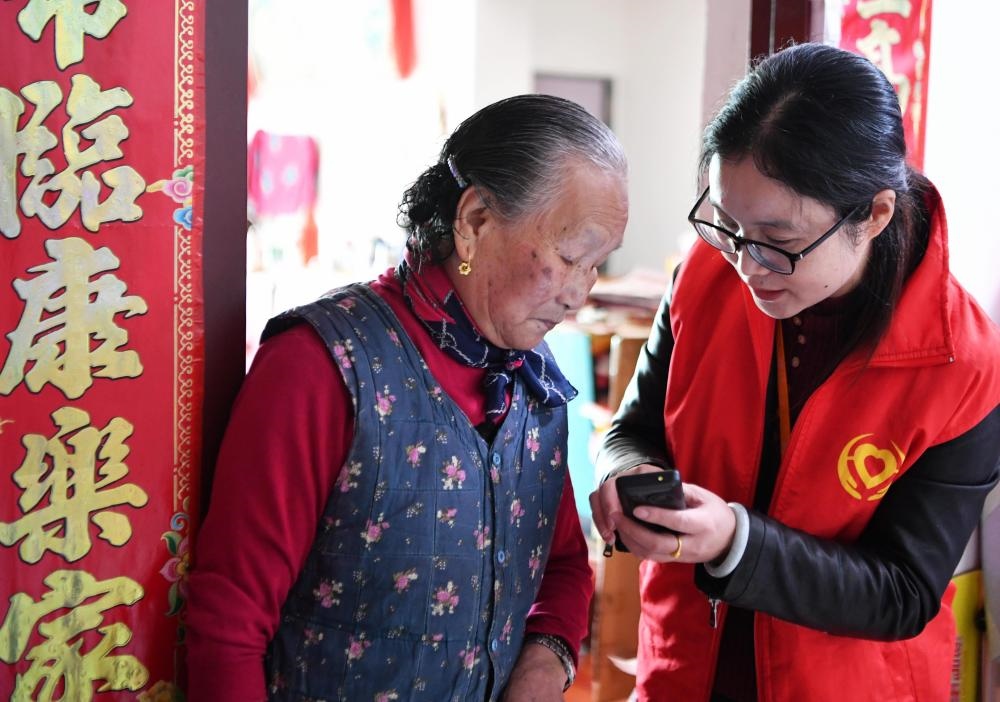 在福州市長樂區(qū)航城街道籌岐村，智慧養(yǎng)老平臺派駐社區(qū)的助老員（右）在為老人陳鳳英（左）講解養(yǎng)老定制手機的用法（2021年11月26日攝）。新華社記者 魏培全 攝