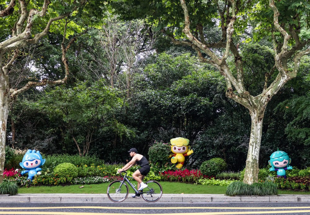 市民在杭州市南山路上一處亞運會主題吉祥物雕塑前騎自行車。