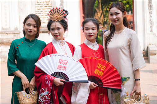 身穿古裝的中國游客和身穿越南傳統(tǒng)服飾奧黛的越南青年在文廟門前合影。