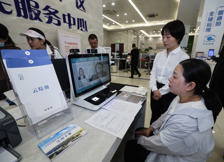 在浙江省嘉興市秀洲區(qū)王江涇鎮(zhèn)便民服務中心的“跨域通辦·云綜窗”窗口，辦理開業(yè)登記的個體工商戶（右一）通過該系統(tǒng)與江蘇省蘇州市吳江區(qū)盛澤鎮(zhèn)行政審批局工作人員視頻連線，進行身份讀取及材料線上審核（2024年5月9日攝）。新華社記者 徐昱 攝