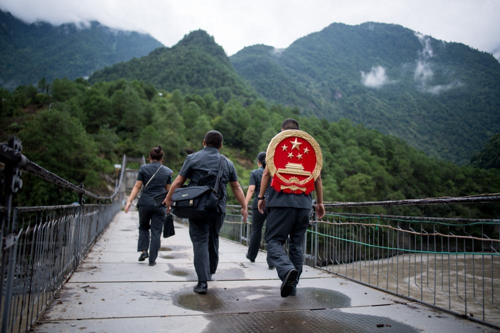 云南省怒江傈僳族自治州貢山縣人民法院法官鄧興背著國(guó)徽與同事們跨過(guò)怒江（2019年8月30日攝）。怒江高山峽谷眾多，交通不便，為方便群眾、更好地開(kāi)展法律服務(wù)，背著國(guó)徽攀高山、過(guò)索橋、躲落石、鉆老林……成為鄧興法官的工作常態(tài)。新華社記者 江文耀 攝