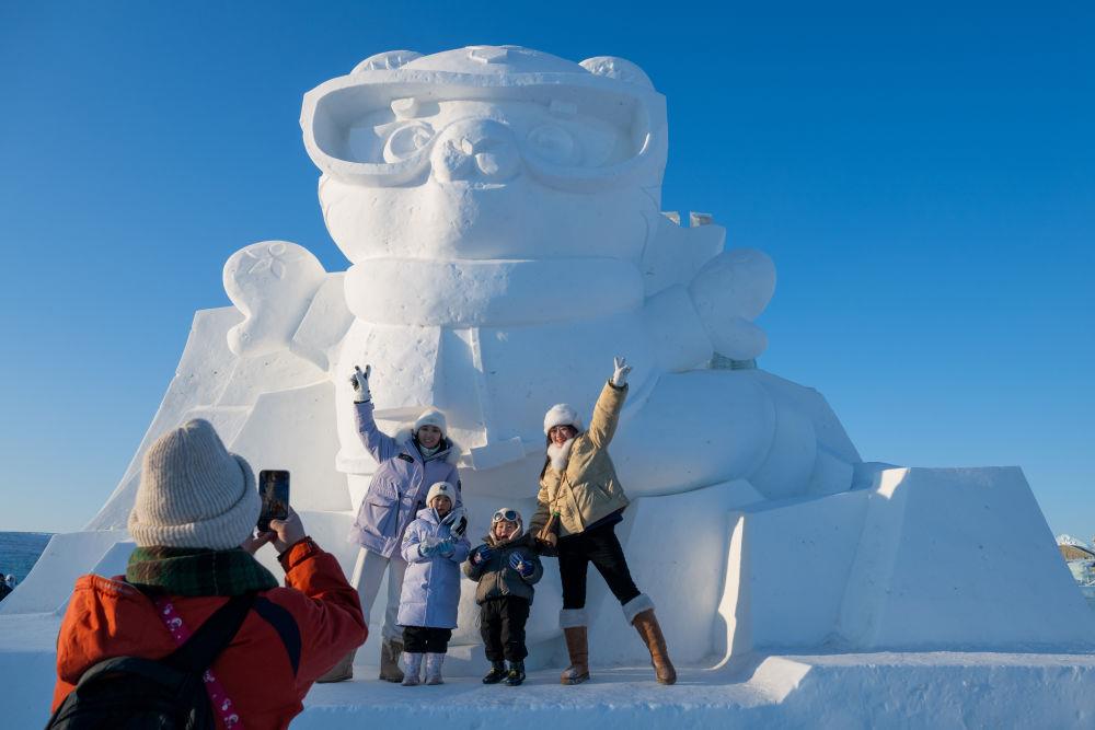 2025年1月3日，在黑龍江哈爾濱冰雪大世界園區(qū)，游客與亞冬會吉祥物雪雕“濱濱”合影